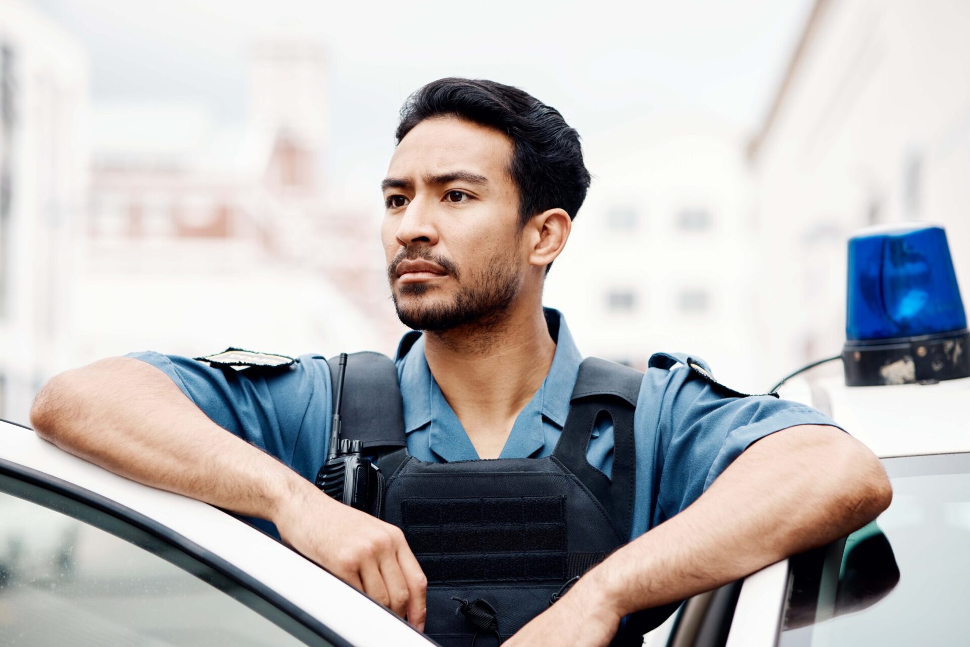 A confident security guard in uniform standing by a patrol car with a serious expression.