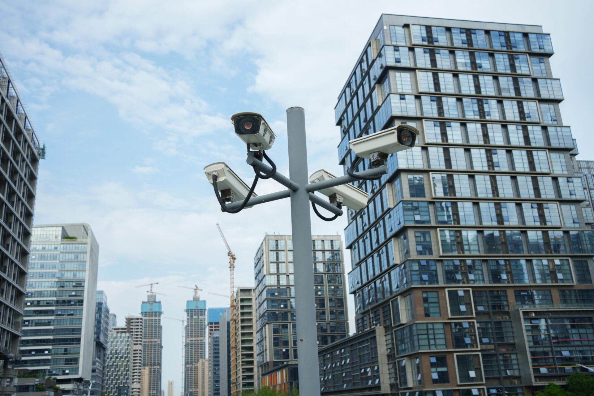 Multiple security cameras mounted on a pole in a modern urban area with tall glass buildings in the background.